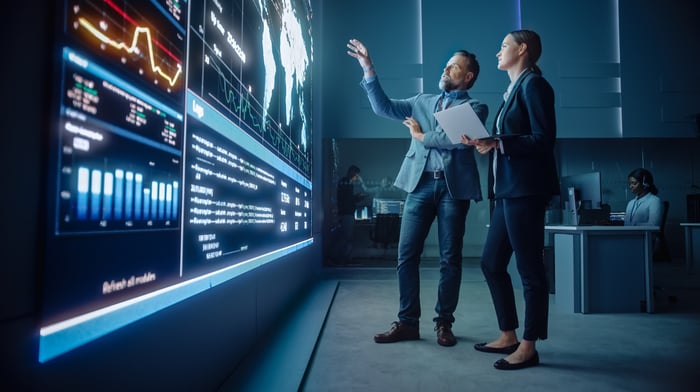 Project Manager and Computer Science Engineer Talk while Using Big Screen Display